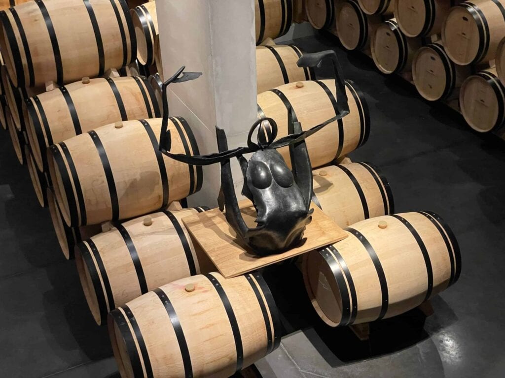 Zeitgenössische Skulptur aus schwarzem Metall im Weinkeller von Château Pédesclaux in Pauillac, umgeben von Eichenfässern zur Reifung von Weinen, Grand Cru Classé aus dem Médoc, Bordeaux.