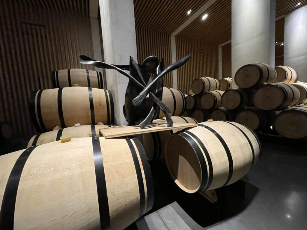 Zeitgenössische Skulptur aus schwarzem Metall im Weinkeller von Château Pédesclaux in Pauillac, umgeben von Eichenfässern zur Reifung von Weinen, Grand Cru Classé aus dem Médoc, Bordeaux.