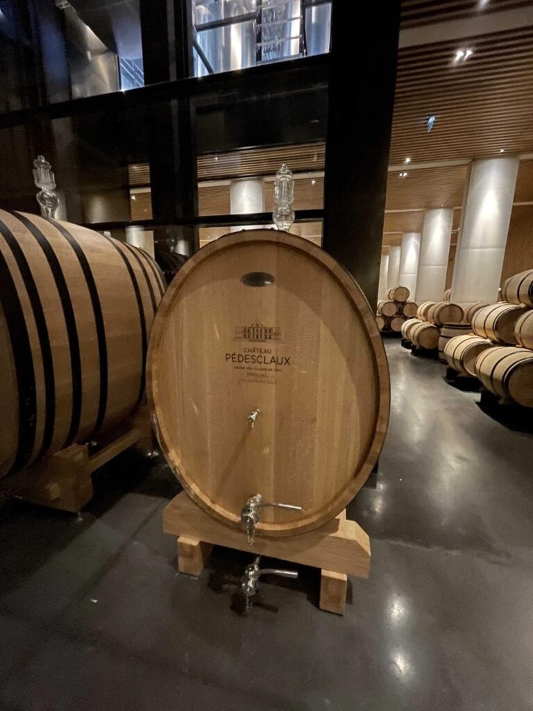 Ein großes Eichenfass mit der Gravur «Château Pédesclaux» im Weinkeller von Pauillac, Bordeaux, Grand Cru Classé des Médoc, umgeben von anderen Fässern zur Reifung prestigeträchtiger Weine.