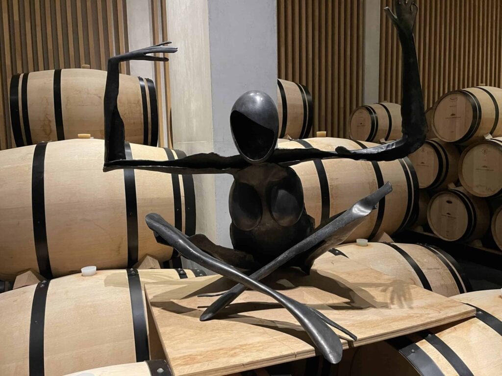 Zeitgenössische Skulptur aus schwarzem Metall im Weinkeller von Château Pédesclaux in Pauillac, umgeben von Eichenfässern zur Reifung von Weinen, Grand Cru Classé aus dem Médoc, Bordeaux.