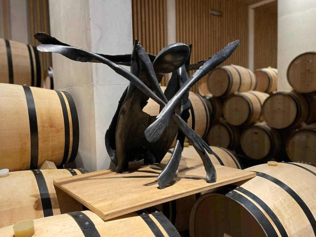 Zeitgenössische Skulptur aus schwarzem Metall im Weinkeller von Château Pédesclaux in Pauillac, umgeben von Eichenfässern zur Reifung von Weinen, Grand Cru Classé aus dem Médoc, Bordeaux.