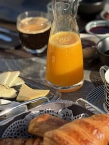 Desayuno completo con zumo de naranja, café, quesos y embutidos.