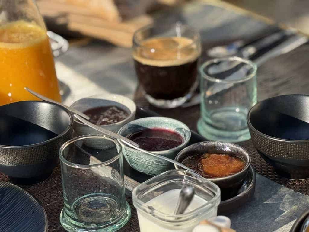 Accueil 14 Table de petit-déjeuner au Château Papounan, Saint-Estèphe, Médoc : assortiment de confitures maison, café, jus d’orange frais et vaisselle élégante, dans une chambre d’hôtes de charme au cœur du vignoble bordelais