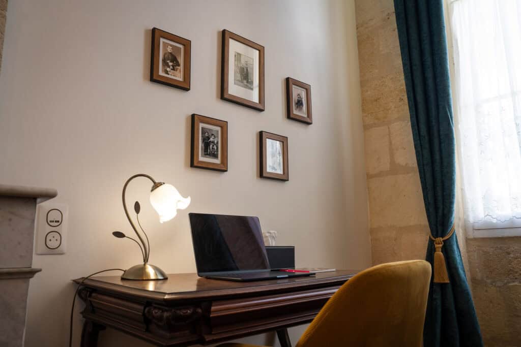 Petit bureau en bois avec lampe rétro et cadres décoratifs dans la Chambre Domeyne du Château Papounan, chambre d’hôtes de charme à Saint-Estèphe, Médoc.