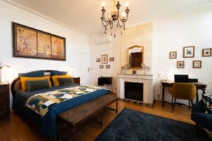 Chambre spacieuse de 27m² au charme rétro avec lit de 160, cheminée en pierre, bureau d'époque, parquet ancien et lustre vénitien au Château Papounan à Saint-Estèphe. Située au rez-de-chaussée avec accès par l'escalier double d'honneur.