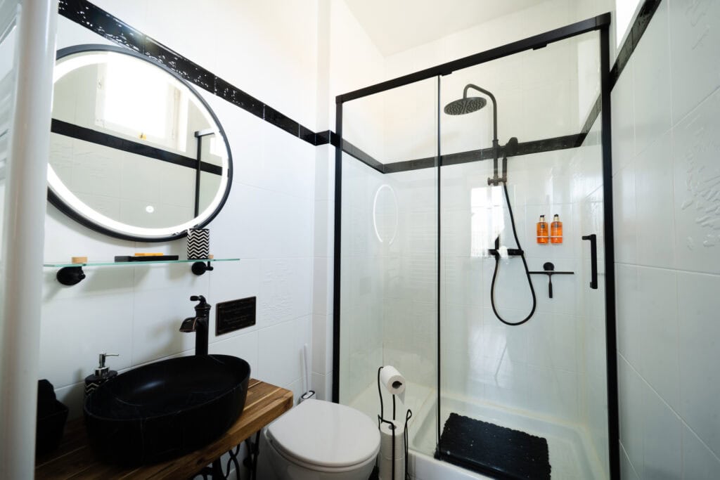 Salle d’eau élégante en noir et blanc dans la Chambre Domeyne du Château Papounan, avec vasque noire sur plan en bois, WC et douche thermostatique à paroi vitrée, dans une chambre d’hôtes de charme à Saint-Estèphe, Médoc.