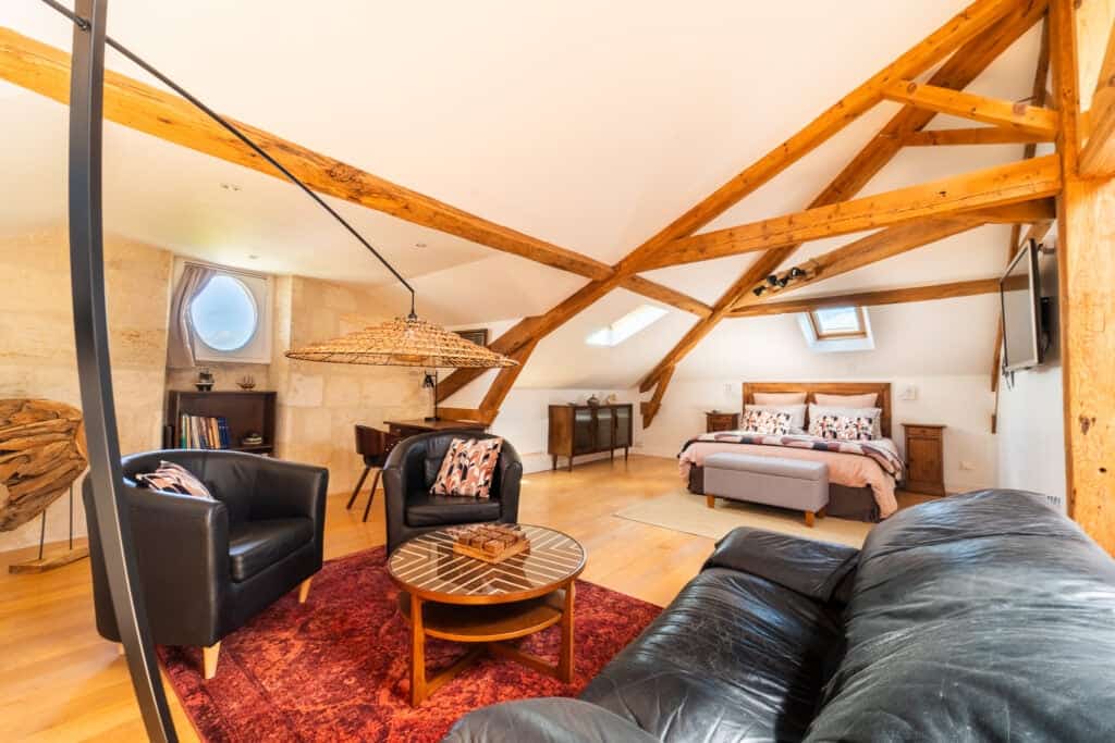 Vue intérieure de la Suite l’Estuaire avec lit queen-size, coin salon, poutres apparentes et décoration raffinée au Château Papounan, chambre d’hôtes de charme à Saint-Estèphe, Médoc.