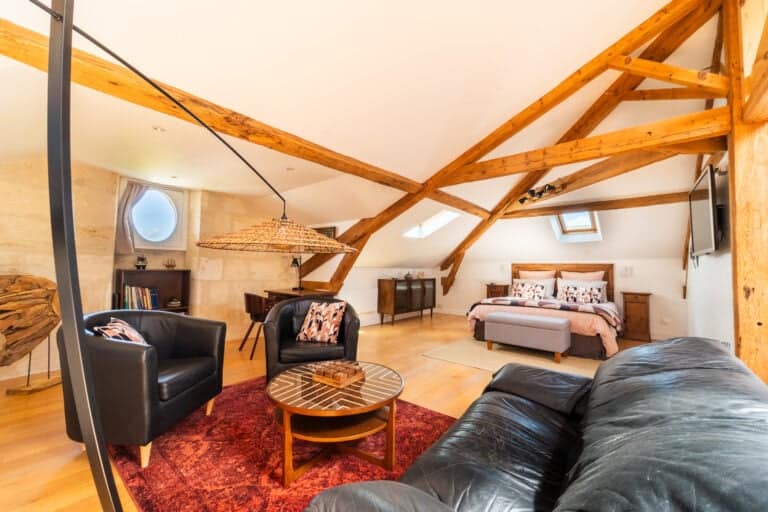 Vista interior de la Suite Estuario con cama queen-size, zona de estar, vigas a la vista y decoración refinada en el Château Papounan, encantador bed and breakfast en Saint-Estèphe, Médoc.