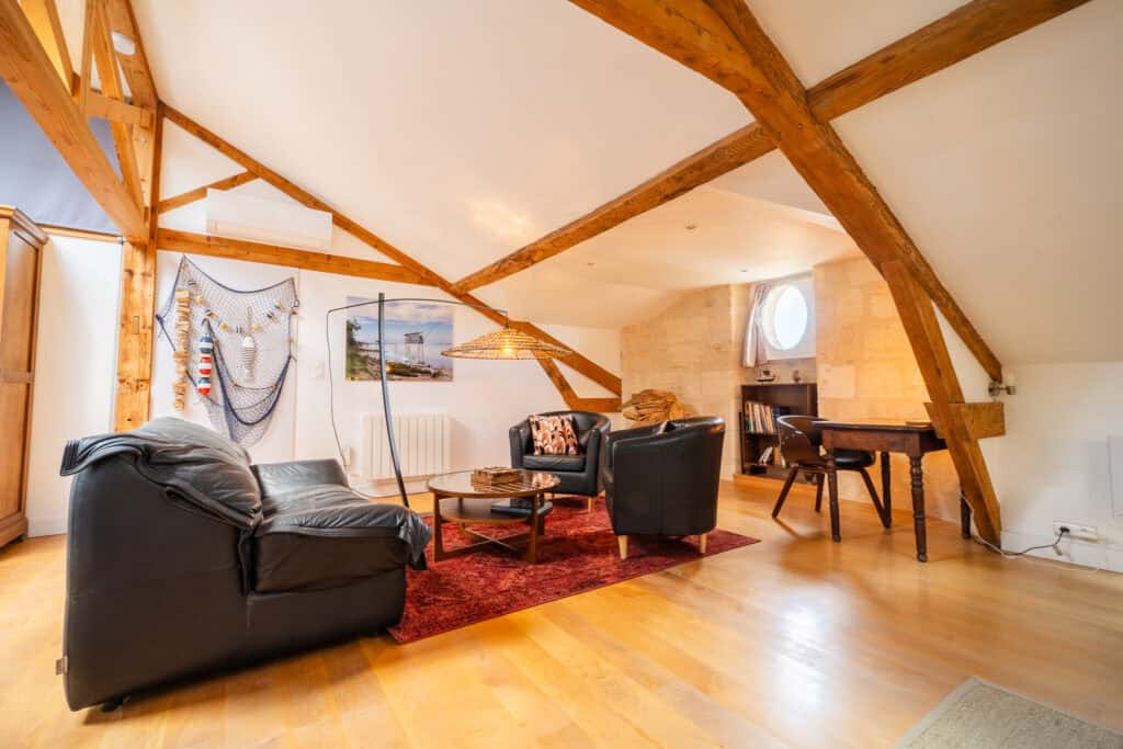 Coin salon élégant avec fauteuils en cuir, table basse et poutres apparentes dans la Suite l’Estuaire du Château Papounan, chambre d’hôtes de charme à Saint-Estèphe, Médoc.