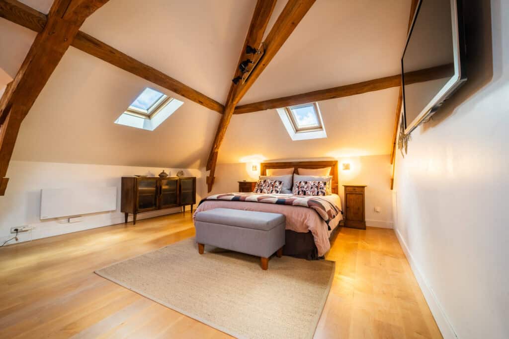 Lit queen-size avec linge en lin et coton sous poutres apparentes dans la Suite l’Estuaire du Château Papounan, chambre d’hôtes de charme à Saint-Estèphe, Médoc.