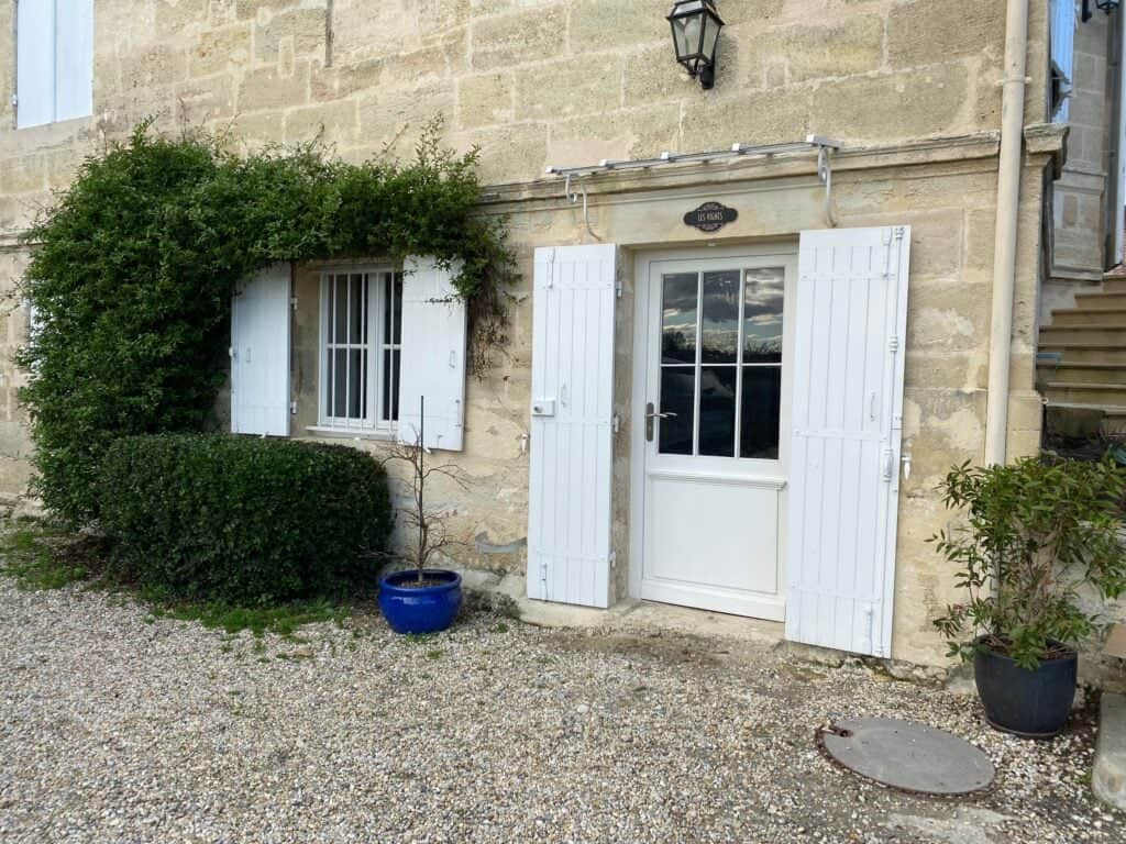 Entrée en rez-de-jardin du Studio Les Vignes avec façade en pierre et volets blancs au Château Papounan, chambre d’hôtes de charme à Saint-Estèphe, Médoc.
