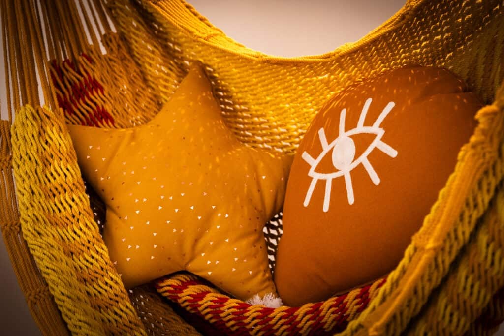 Hamac jaune avec coussins décoratifs en forme d’étoile et motif œil dans la Suite Océane du Château Papounan, chambre d’hôtes de charme à Saint-Estèphe, Médoc.