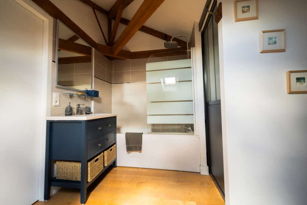 Salle de bain élégante avec poutres apparentes, meuble vasque bleu et baignoire dans la Suite Océane du Château Papounan, chambre d’hôtes de charme à Saint-Estèphe, Médoc.