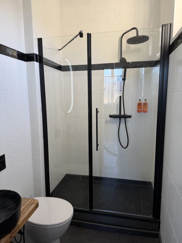 Chambres d'hôtes dans un espace douche moderne et noir, vitrage et WC visibles.